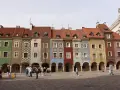 Kolorowe kamienice na Starym Rynku w Poznaniu, wspaniałe poznan atrakcje. Ludzie spacerują po brukowanym placu.