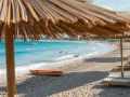 Słoneczny dzień na plaży Nissi Beach. Leżaki pod parasolami, turkusowa woda, kajak i ludzie kąpiący się w morzu.