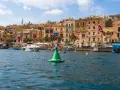Malta w sierpniu: port z łodziami i kamiennymi budynkami, ozdobiony flagami.