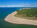 Plaża i las na Helu. Widok z lotu ptaka na turkusowe morze, piaszczystą plażę i zielony las. W oddali widać zabudowania i port. Hel atrakcje czekają!