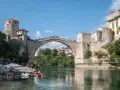 Mostar, Bośnia i Hercegowina: Słynny Stary Most z kamienia, tłumy ludzi na moście i brzegu, łodzie na rzece Neretwie.