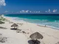 Pusta, piaszczysta nordeste playa z turkusową wodą i dwoma słomianymi parasolami. Kobieta spaceruje brzegiem morza.