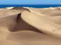 Pofaśne wydmy Maspalomas tworzą pustynny krajobraz, gdzie piasek faluje ku błękitnemu oceanowi.