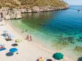 Sycylia pogoda idealna na plażowanie. Słoneczny dzień, turkusowa woda i kamienista plaża z kilkoma osobami relaksującymi się pod parasolami.