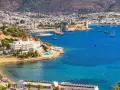 Piękna pogoda w Bodrum w Turcji. Białe budynki hotelowe, basen, plaża i zatoka pełna łodzi na tle wzgórz.