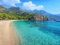Piękna plaża w Turcji, Kusadasi, z turkusową wodą, górami i sosnami. Idealne miejsce na wakacje.