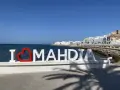 Napis "I ❤️ MAHDIA" na tle morza i białych budynków. Słońce i cień palm. Tunezja Mahdia.