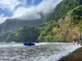 Surfer z niebieską deską na seixal beach, w tle zielone klify i chmury.