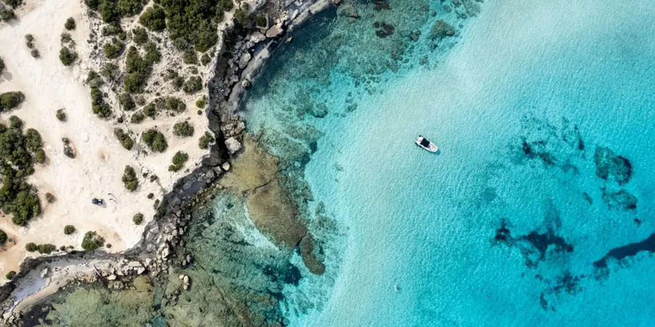 Plaża z turkusową wodą i łodzią, skaliste wybrzeże. Czy to Pafos czy Larnaka?