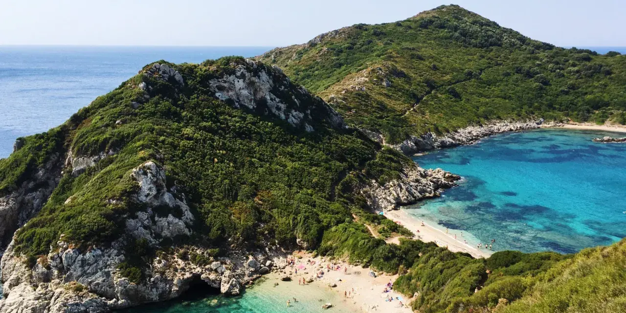 Malownicza zatoka z piaszczystą plażą na Korfu, otoczona zielonymi wzgórzami i krystalicznie czystą wodą.