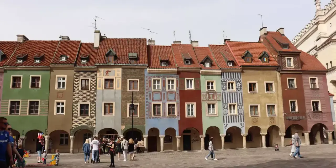 Kolorowe kamienice na Starym Rynku w Poznaniu, wspaniałe poznan atrakcje. Ludzie spacerują po brukowanym placu.