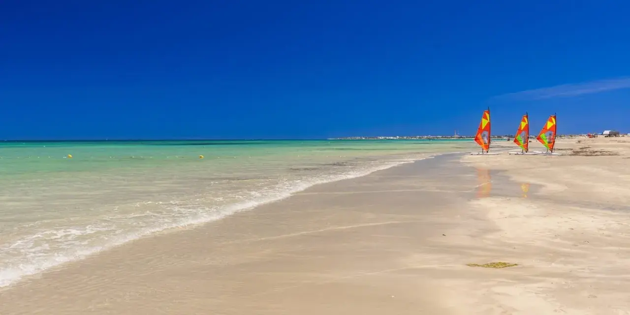 Piękna, słoneczna plaża w Tunezji we wrześniu. Trzy kolorowe żagle desek do windsurfingu stoją na piasku.