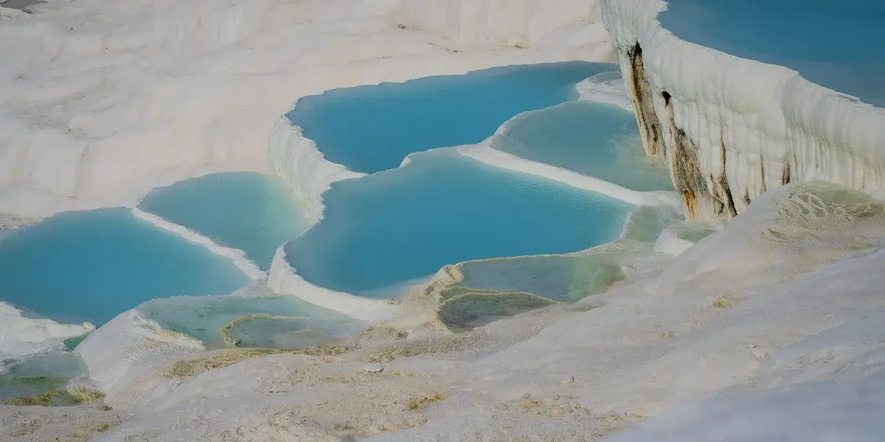 Turkusowe wody tworzą kaskady na białych tarasach wapiennych w Pamukkale w Turcji.