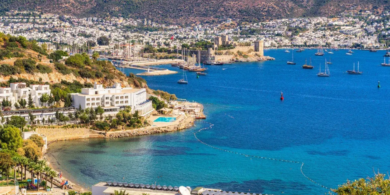 Piękna pogoda w Bodrum w Turcji. Białe budynki hotelowe, basen, plaża i zatoka pełna łodzi na tle wzgórz.