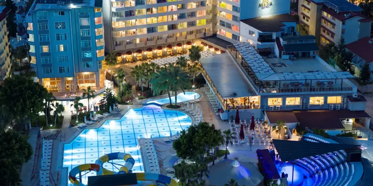 Nocny widok na Meridia Beach Hotel z oświetlonymi basenami, zjeżdżalniami i restauracją.
