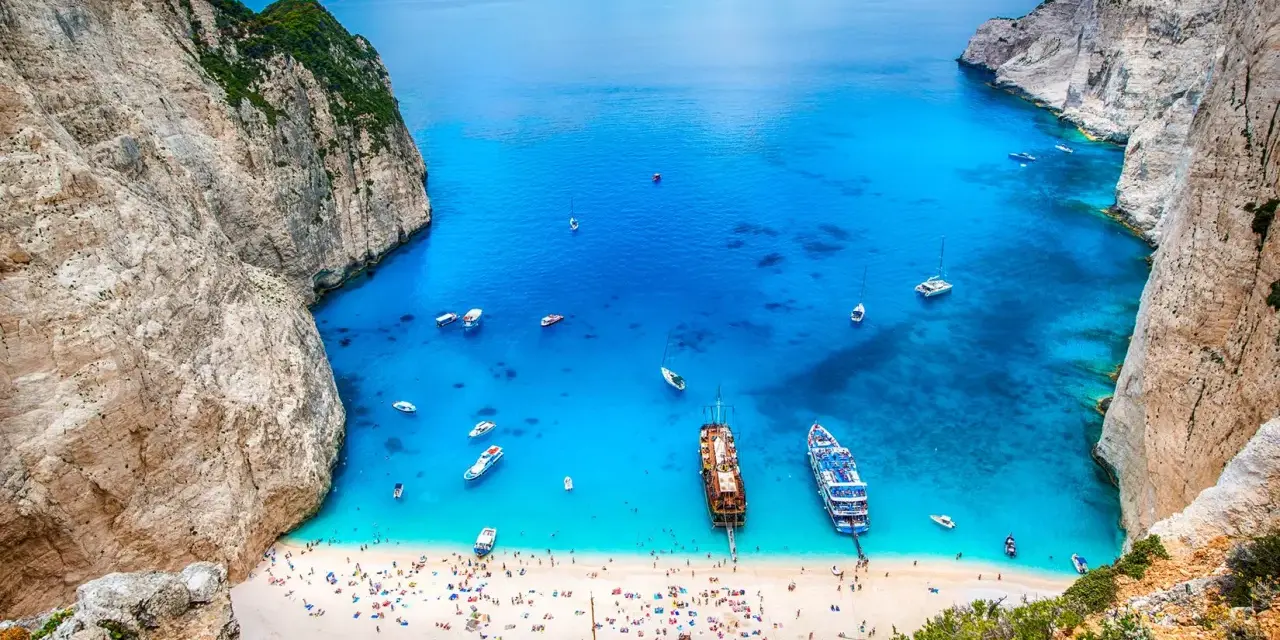 Zatoka Navagio, najcieplejsza wyspa grecka, z turkusową wodą, białym piaskiem, statkami i wrakiem.