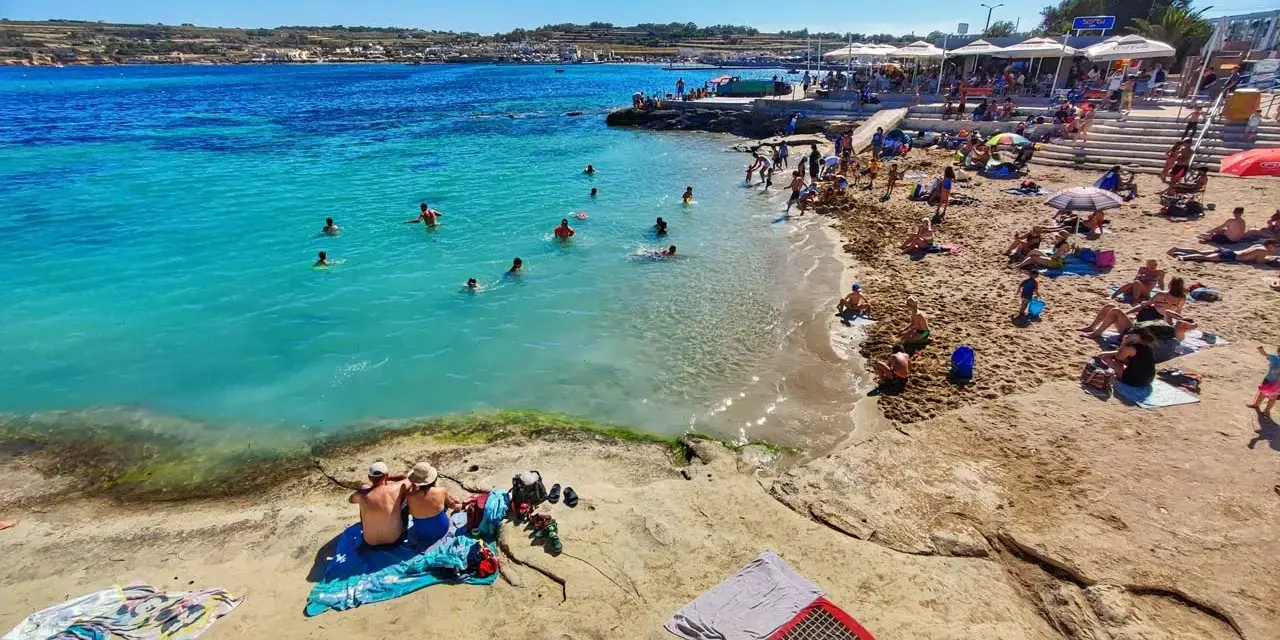 Słoneczna plaża na Malcie, ludzie kąpią się w turkusowej wodzie. Idealna temperatura do opalania i pływania.