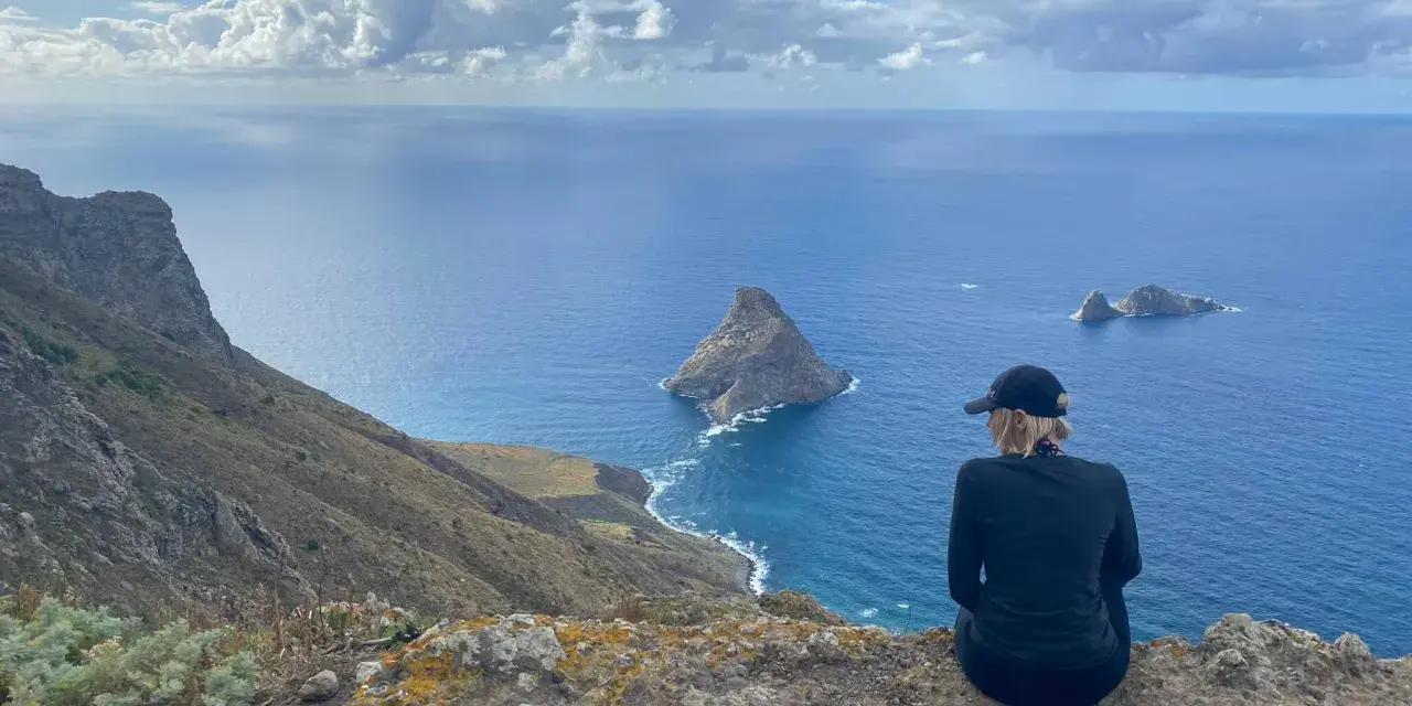 Widok na ocean z klifu, idealna teneryfa pogoda w grudniu. Kobieta w czapce podziwia skaliste wysepki.