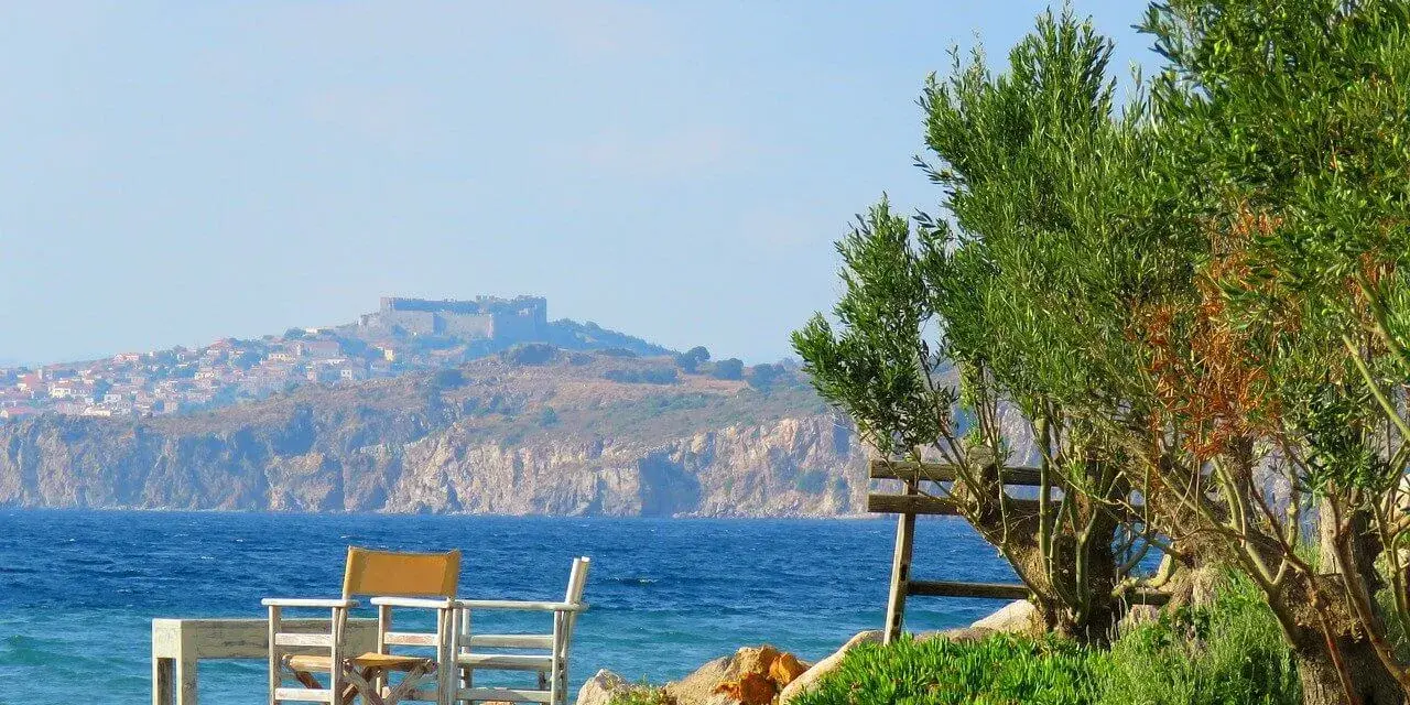 Piękna pogoda na Lesbos. Stół i krzesła czekają na plaży, w tle widać zamek i miasteczko.