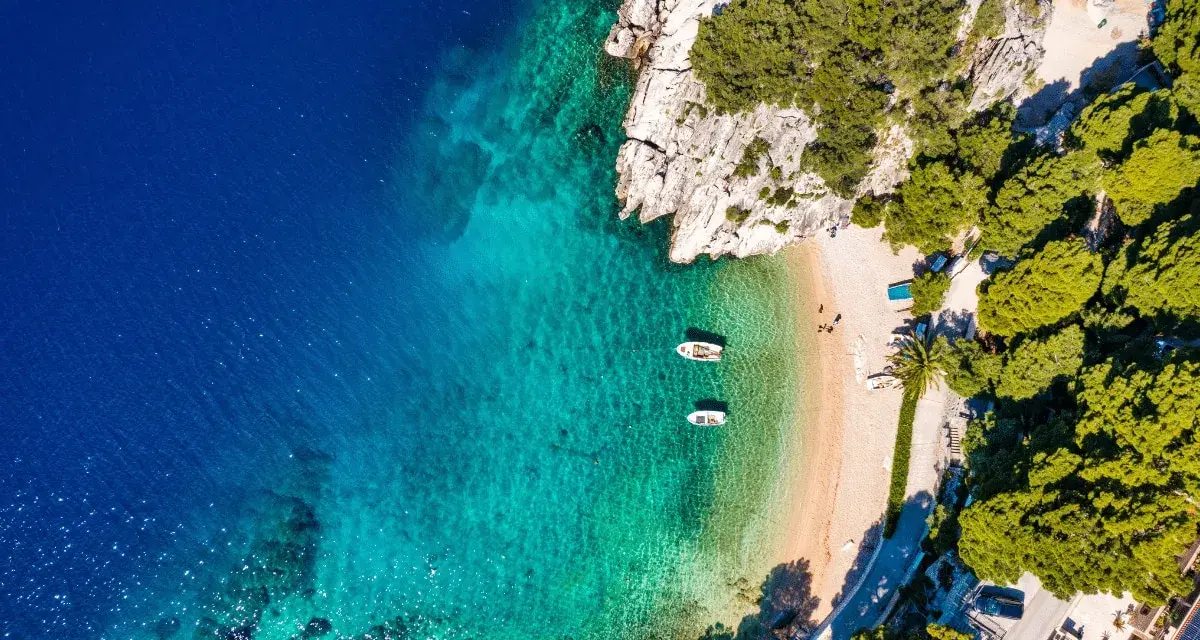 Widok z lotu ptaka na zatokę z krystalicznie czystą wodą, piaszczystą plażą i łodziami. Idealne miejsce na wakacje, jak z pocztówki z Chorwacji.