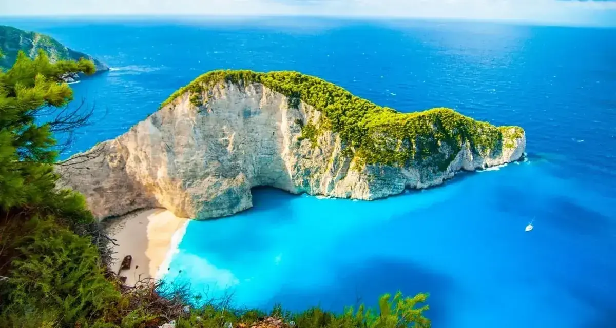 Grecja w kwietniu zachwyca pogodą. Widok na Navagio Beach z klifu, turkusowe morze i biały piasek.