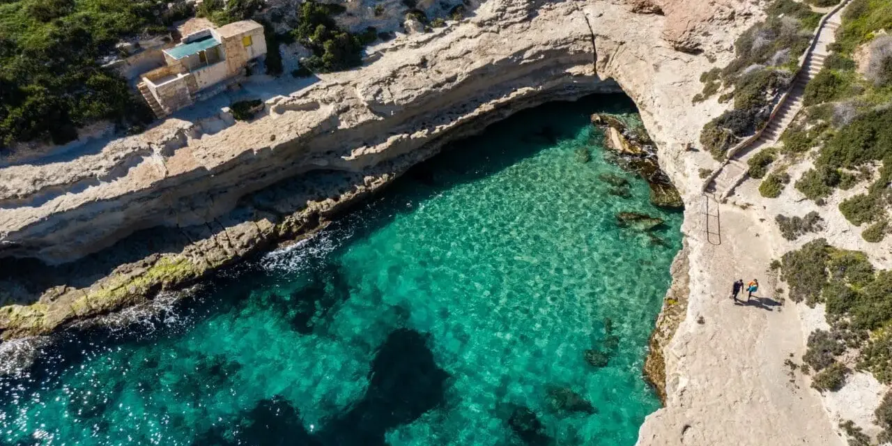 Malta plaza: turkusowa woda w zatoce, skaliste klify i schody prowadzące do ukrytej plaży.