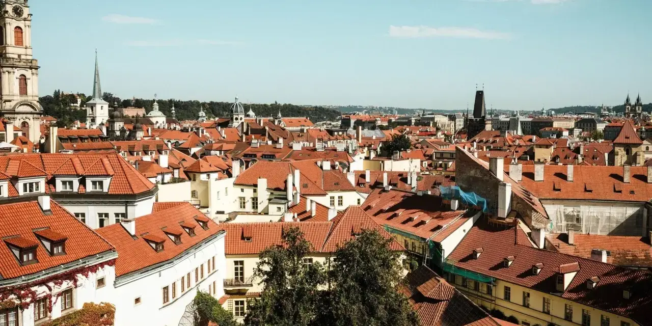 Widok na dachy Pragi, idealne miejsce na city break. W oddali wieże kościołów i wieża zegarowa.