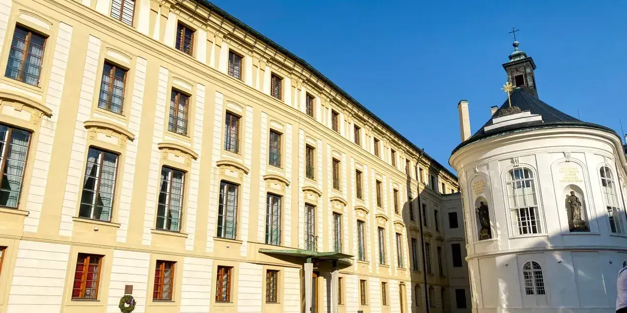 Zamek na Hradczanach, z jego żółtą fasadą i białą, okrągłą kaplicą, prezentuje się majestatycznie pod błękitnym niebem.