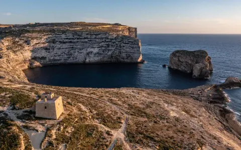 Malta pogoda w styczniu: słoneczny dzień nad zatoką z wieżą strażniczą i skalistymi klifami.
