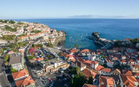 Widok na miasteczko Camara de Lobos z licznymi łodziami w zatoce. Domy z czerwonymi dachami schodzą ku morzu.