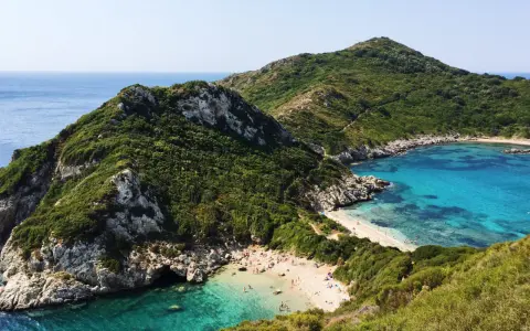 Malownicza zatoka z piaszczystą plażą na Korfu, otoczona zielonymi wzgórzami i krystalicznie czystą wodą.