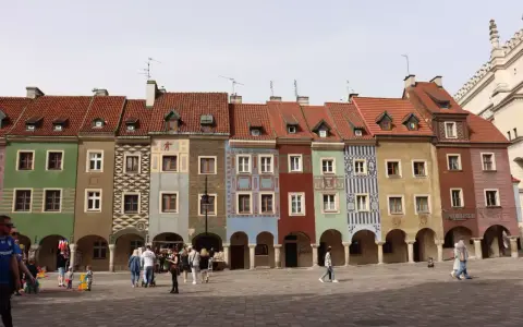 Kolorowe kamienice na Starym Rynku w Poznaniu, wspaniałe poznan atrakcje. Ludzie spacerują po brukowanym placu.