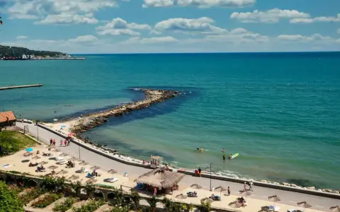 Piękna pogoda w maju w Bułgarii. Słoneczny dzień nad turkusowym morzem, plaża z leżakami i parasolami, ludzie kąpią się i spacerują.