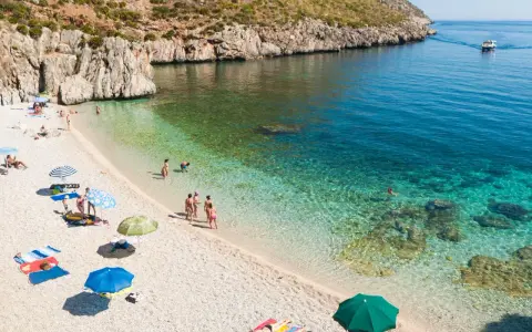 Sycylia w październiku: kamienista plaża, turkusowa woda, ludzie odpoczywają pod parasolami.