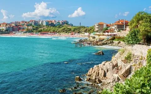 Słoneczna plaża i turkusowe morze w Bułgarii. Widok na miasteczko z czerwonymi dachami i skaliste wybrzeże z kamiennymi schodami. Atrakcje turystyczne nad Morzem Czarnym.