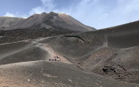 Grupa turystów wędruje po zboczach wulkanu Etna, podziwiając surowy krajobraz i dymiący krater.