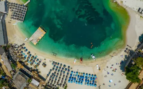 Widok z lotu ptaka na plażę w Albanii. Turkusowa woda, leżaki, parasole i łodzie. Idealne miejsce na albania wakacje 2026.