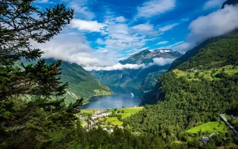 Majestatyczne fiordy Norwegii, z zielonymi zboczami gór, błękitnym niebem i statkiem wycieczkowym na wodzie.