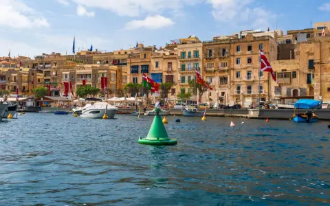 Malta w sierpniu: port z łodziami i kamiennymi budynkami, ozdobiony flagami.