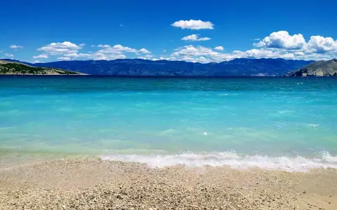 Idealne miejsce, gdzie lecieć w czerwcu: turkusowe morze, kamienista plaża i góry w tle.