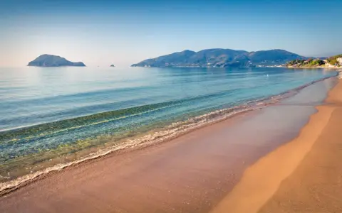 Spokojna plaża Caretta z łagodnymi falami i wyspami w oddali. Idealne miejsce na relaks.