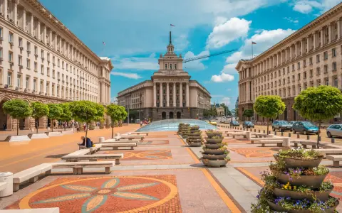 Słoneczna pogoda w Bułgarii w lipcu. Sofia, plac przed budynkiem Narodowego Zgromadzenia, z drzewami i kwiatami.