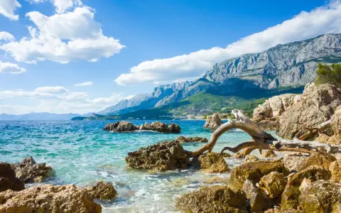 Piękne wybrzeże Chorwacji z turkusową wodą, skalistą plażą i górzystym krajobrazem w tle. Idealne miejsce, by zastanowić się, gdzie do Chorwacji.