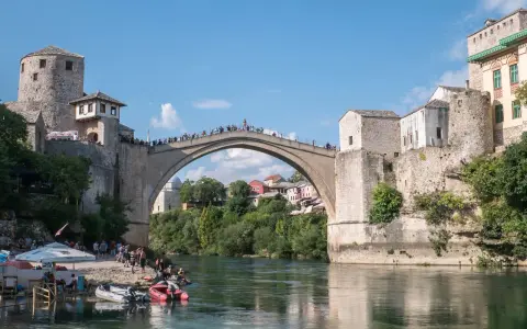 Mostar, Bośnia i Hercegowina: Słynny Stary Most z kamienia, tłumy ludzi na moście i brzegu, łodzie na rzece Neretwie.