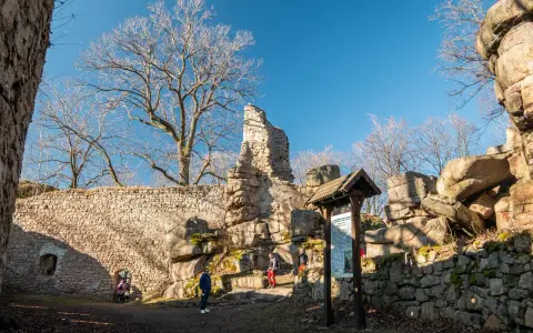 Ruiny zamku na rudawach janowickich. Kamienne mury, skalne formacje i nagie drzewa pod błękitnym niebem.