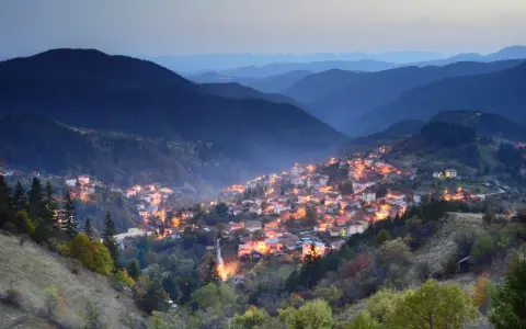 Wieczorna panorama urokliwej wioski w bułgarskim pasmie górskim, oświetlonej ciepłym blaskiem okien.