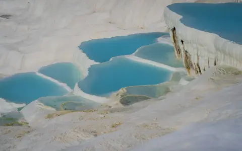 Turkusowe wody tworzą kaskady na białych tarasach wapiennych w Pamukkale w Turcji.
