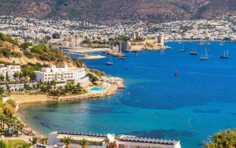 Piękna pogoda w Bodrum w Turcji. Białe budynki hotelowe, basen, plaża i zatoka pełna łodzi na tle wzgórz.