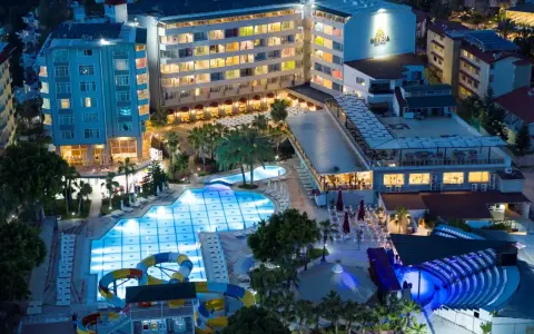 Nocny widok na Meridia Beach Hotel z oświetlonymi basenami, zjeżdżalniami i restauracją.