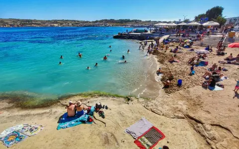 Słoneczna plaża na Malcie, ludzie kąpią się w turkusowej wodzie. Idealna temperatura do opalania i pływania.